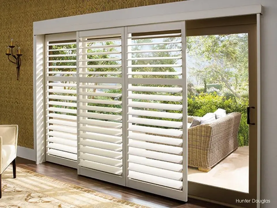 Hunter Douglas Palm Beach shutters open in bypass position on a sliding glass door in a living room